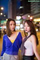 Two young women standing next to each other on a city street.