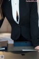 A woman in a black suit sitting at a desk with a laptop.