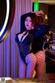 A woman in a black bodysuit and fishnet stockings posing in front of a mirror.