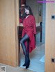 A woman in a red coat and black tights standing in a doorway.