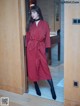 A woman standing in front of a wooden door wearing a red coat.