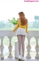 A woman in a yellow sweater and white skirt standing on a balcony.