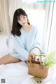 A woman sitting on a bed holding a basket of plants.