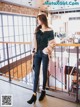 A woman standing on a balcony in a black top and jeans.