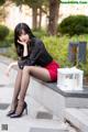 A woman in a black shirt and red skirt sitting on a ledge.