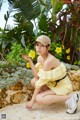 A woman in a yellow dress and a baseball cap crouching down with a flower.