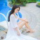 A woman in a white dress sitting by a swimming pool.