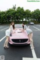 A couple of women standing next to a pink car.