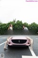 A couple of women sitting on top of a pink car.