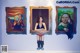 A woman standing in front of three paintings on a wall.