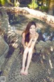 A woman in a pink bikini sitting on a rock by a pool.