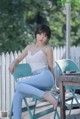 A woman sitting on a blue chair in front of a white fence.